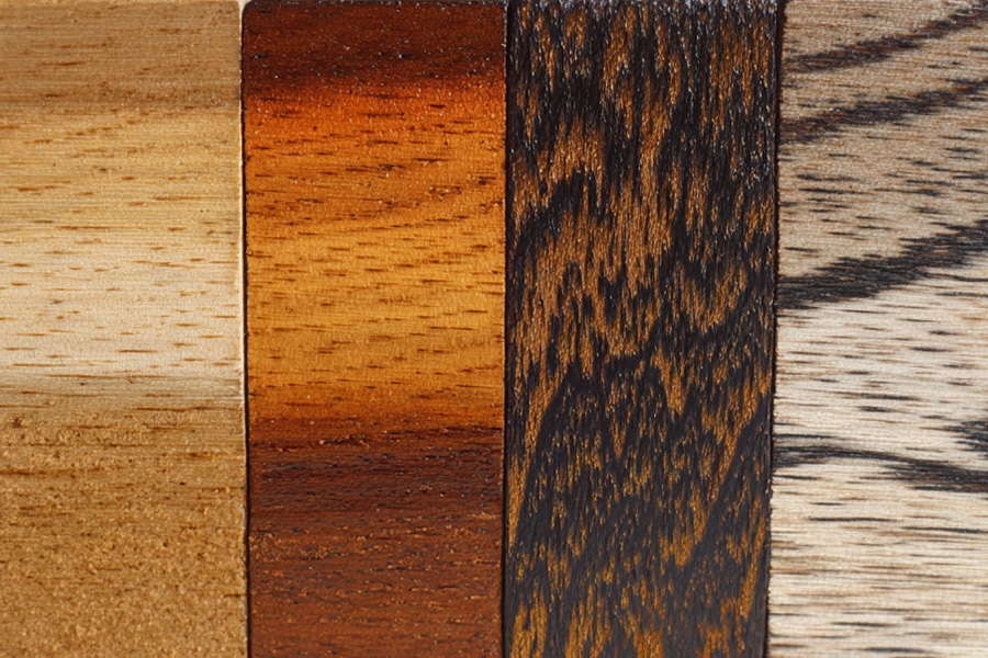 Four vertical wooden panels, each with a different color and grain pattern, ranging from light beige to dark brown and black streaks, showcasing various types of wood finishes.